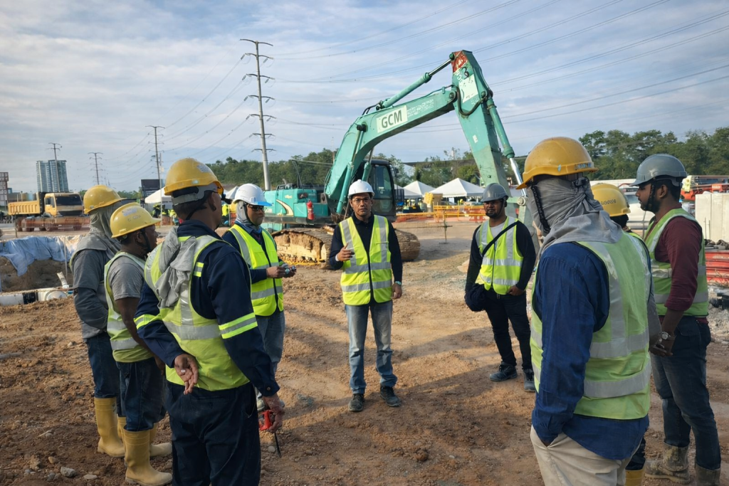 GCM site team conducting safety briefing at construction project site with excavator support